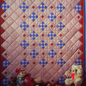 Peut inclure: Une courtepointe avec un motif en losange dans des tons de rose, rouge et bleu. Deux ours en peluche sont assis dans des fauteuils à bascule devant la courtepointe. Il y a des pommes et un cheval à bascule sur le sol.