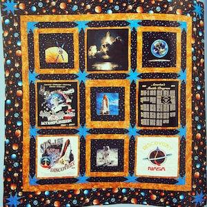 May include: A quilt with a space theme. It features images of the space shuttle, astronauts, planets, and stars. The quilt is made of a variety of fabrics, including black, blue, and orange. The quilt is framed with a blue and orange border.