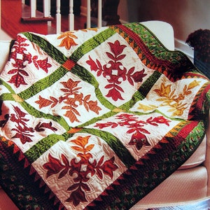 May include: A quilt with a white background and a patchwork design of green, red, and orange leaves. The quilt is folded and draped over a white sofa.