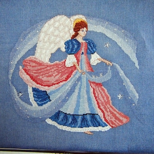 May include: Cross-stitch artwork of an angel in a blue dress with red accents and white wings. The angel has brown hair and a gold halo. The background is a light blue with white stars and a white arc.