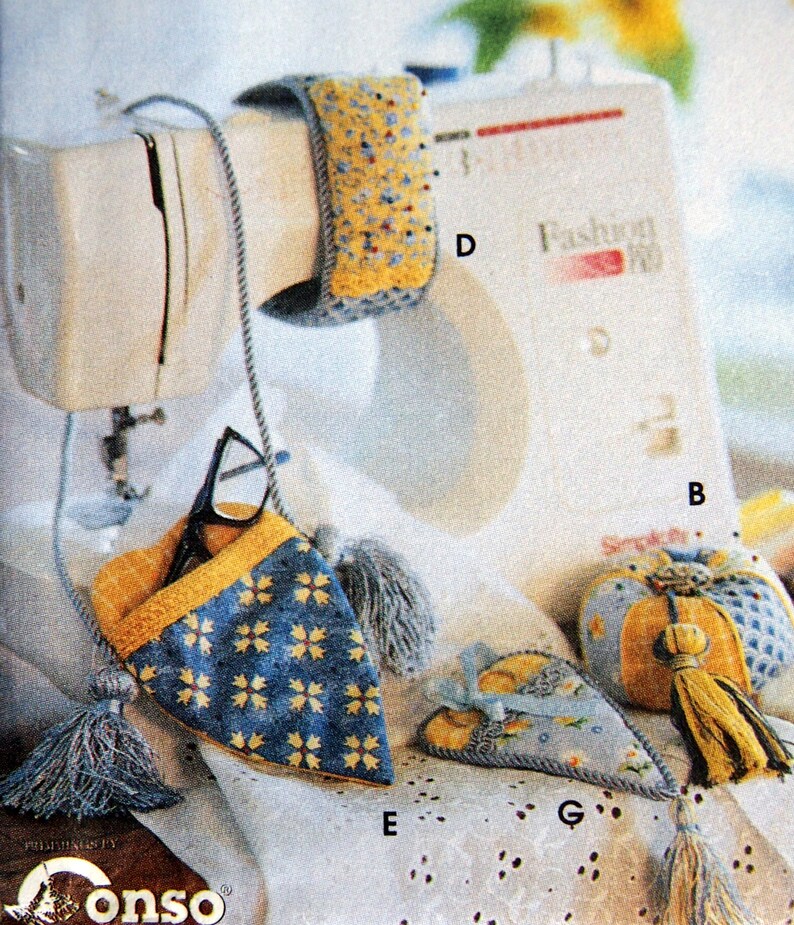 May include: An assortment of handmade fabric accessories, including a glasses case, pincushion, and wrist rest, all featuring blue and yellow floral patterns. Each item is adorned with tassels and decorative stitching.