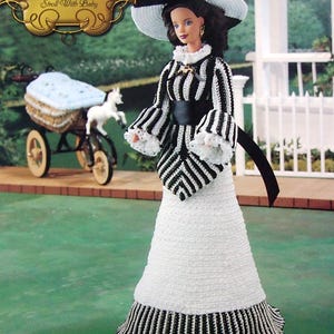 May include: A doll from "The Southern Belle Collection" in a black and white striped dress, a wide-brimmed hat, and a black belt. The doll is on green grass, with a baby carriage and a white picket fence in the background.