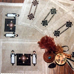 Peut inclure: Quatre sets de table en lin beige avec des motifs brodés en noir et blanc. Les motifs comprennent des motifs géométriques et des figures de personnes portant des robes.