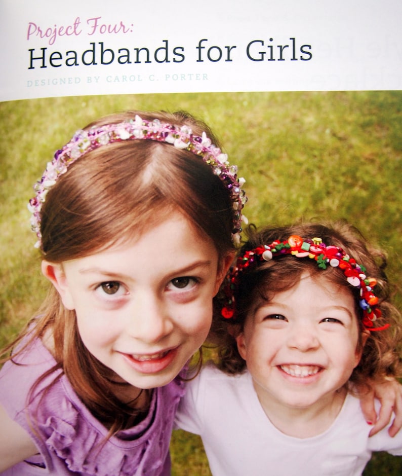 May include: Two girls wearing colorful headbands made with beads and buttons. The headband on the girl in the front is made with pink, white, and purple beads. The headband on the girl in the back is made with red, green, and yellow buttons.
