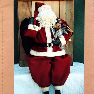 May include: A handcrafted Santa Claus doll in a red suit, white beard, and black boots, holding a teddy bear and a smaller doll. The image includes the text "Threads That Bind" and "Tis The Night".