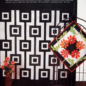 May include: A black and white quilt with a geometric design is displayed on a metal stand. A smaller quilt with orange daisies and green leaves is also shown. The text "Study in Black and White" and "Wild Daisies" are visible.