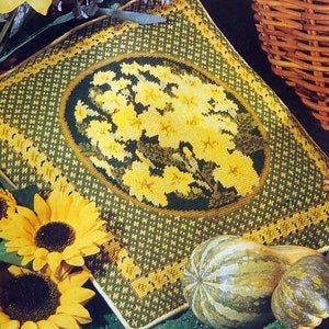 May include: A green and yellow embroidered cushion with a floral design. The cushion is surrounded by sunflowers and a gourd.