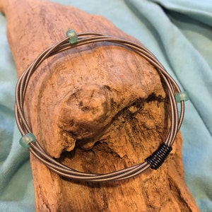 May include: A silver guitar string bracelet with three turquoise beads and a black metal clasp.