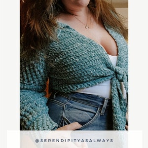 May include: A teal blue crochet sweater with a tie front. The sweater is worn over a white tank top and blue jeans. The text "@serendipityasalways" and "Maise Sweater Crochet Pattern PDF Digital Download" is displayed below the image.