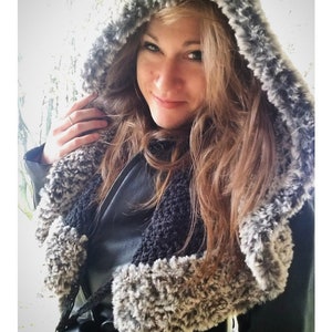 May include: A woman wearing a gray and black hooded crocheted scarf. The scarf has a fluffy texture and is worn over a black jacket. The text "INTUITION HOOD crochet pattern serendipity-as-always.com" is visible at the bottom of the image.
