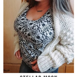 Op de afbeelding: Een wit gebreid vest met een textuurpatroon. Het vest wordt gedragen over een zwart-wit geprint shirt. De tekst "STELLAR MOON crochet pattern" en "serendipity-as-always.com" is zichtbaar onderaan de afbeelding.
