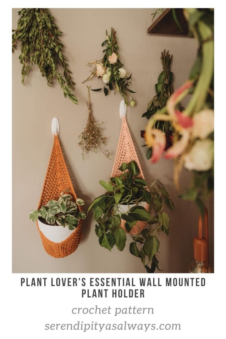 Puede incluir: Dos maceteros colgantes de crochet en naranja y rosa cuelgan de una pared con un gancho blanco. Los maceteros est&aacute;n llenos de plantas en maceta.
