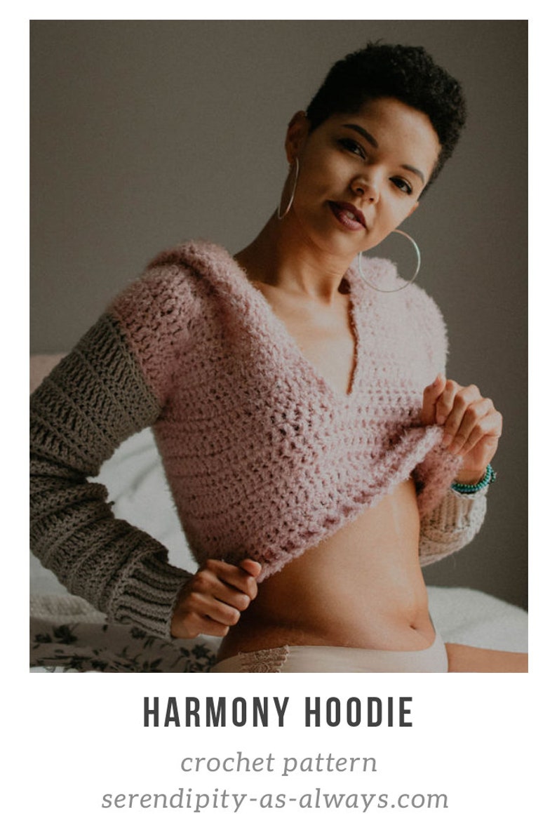 May include: A pink and gray crochet hoodie with a hood. The hoodie is cropped and has a V-neck. The text "HARMONY HOODIE" and "crochet pattern" are visible below the image. The text "serendipity-as-always.com" is visible below the text.