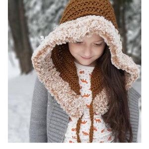 May include: A brown crochet hooded scarf with a white faux fur lining. The hood is pointed and the scarf is tied with a brown cord. The scarf is worn by a child in a snowy setting.