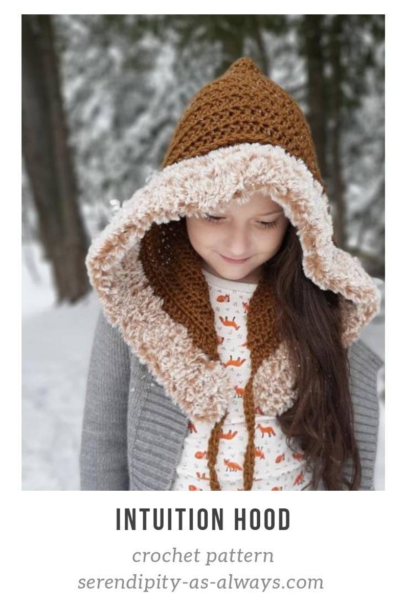 May include: A brown crochet hooded scarf with a white faux fur lining. The hood is pointed and the scarf is tied with a brown cord. The scarf is worn by a child in a snowy setting.