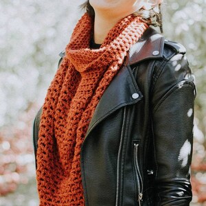 May include: A woman wearing a black leather jacket with a rust-colored crocheted scarf and leopard print mittens.