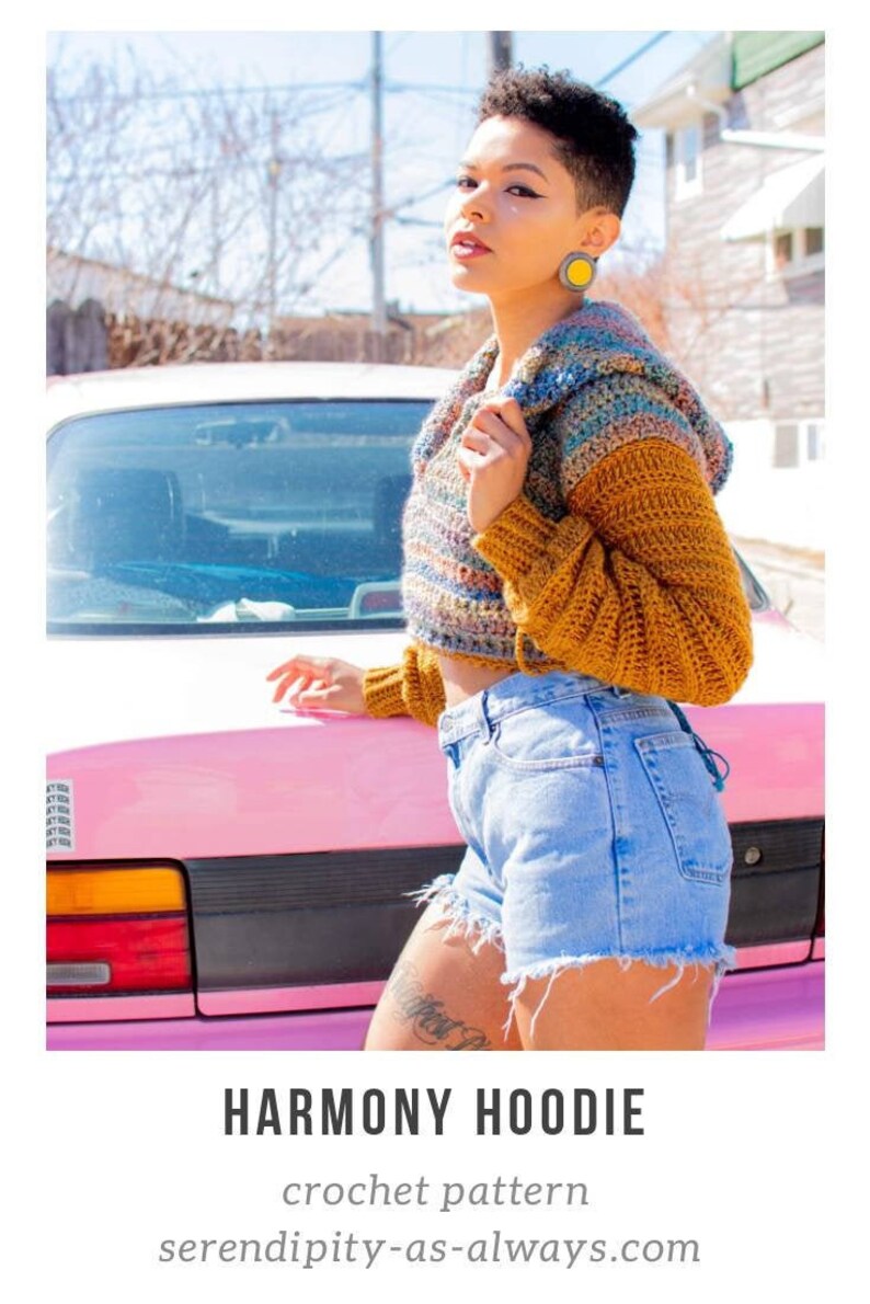 May include: A woman wearing a multi-colored crochet hoodie with a brown crocheted sleeve. The hoodie is cropped and has a hood. She is standing in front of a pink car. The text "HARMONY HOODIE" and "crochet pattern" are visible below the image. The text "serendipity-as-always.com" is visible below the text.