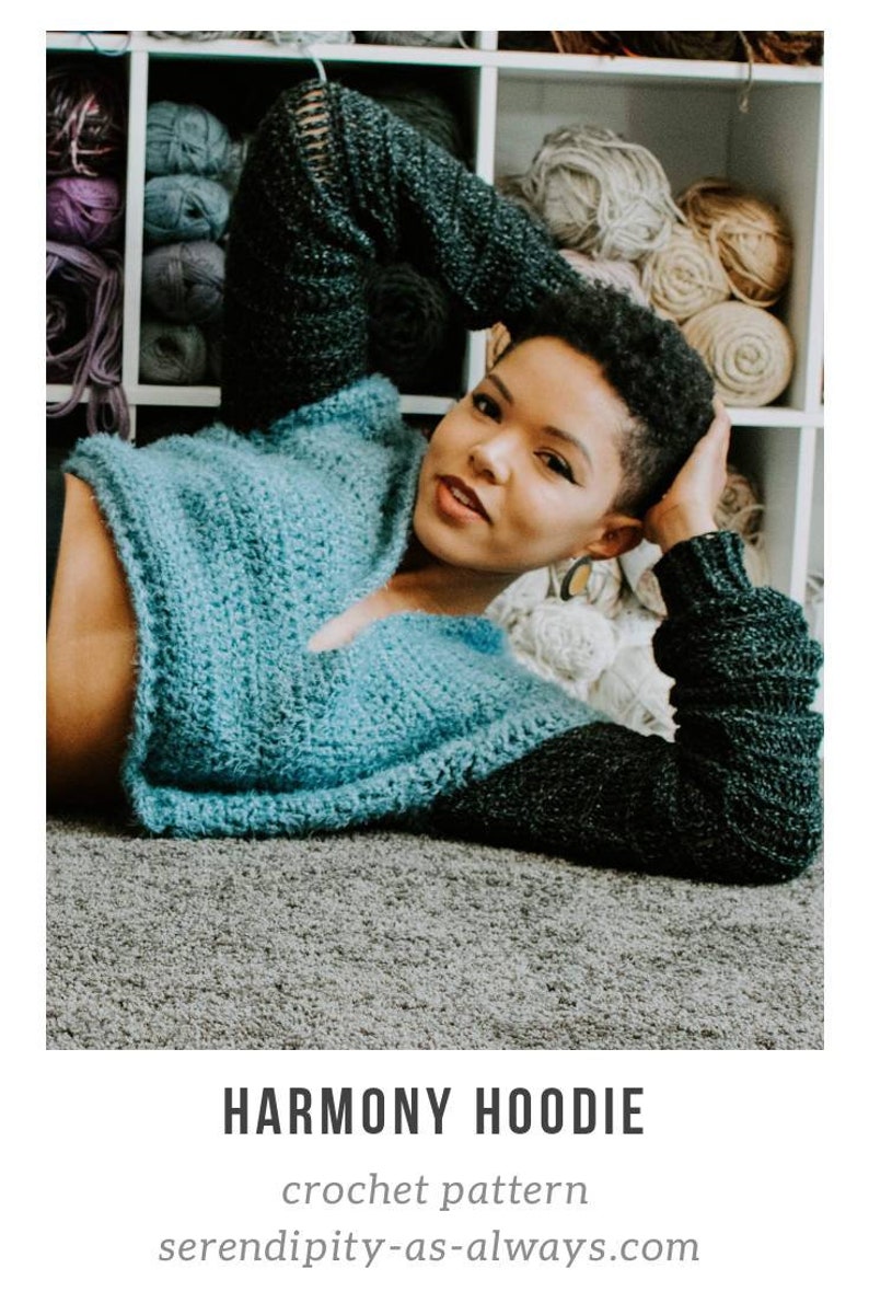 May include: A woman wearing a blue and black crochet hoodie. The hoodie has a V-neck and long sleeves. The woman is lying on a gray carpet. The text "HARMONY HOODIE" and "crochet pattern" is visible below the image. The text "serendipity-as-always.com" is visible below the text.