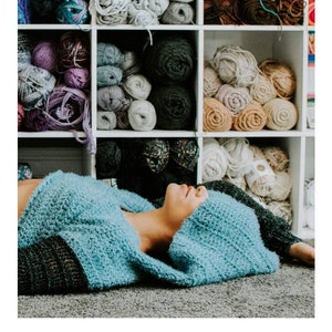 May include: A blue crocheted hoodie with a large hood, lying on a gray surface. The image is accompanied by the text "HARMONY HOODIE crochet pattern serendipity-as-always.com".