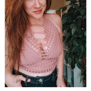 May include: A pink crochet halter top with a cutout design. The top is worn by a person with long brown hair and is paired with blue jeans. The text "GABRIELLE TOP" and "crochet pattern" are visible below the image. The website address "serendipity-as-always.com" is also visible.
