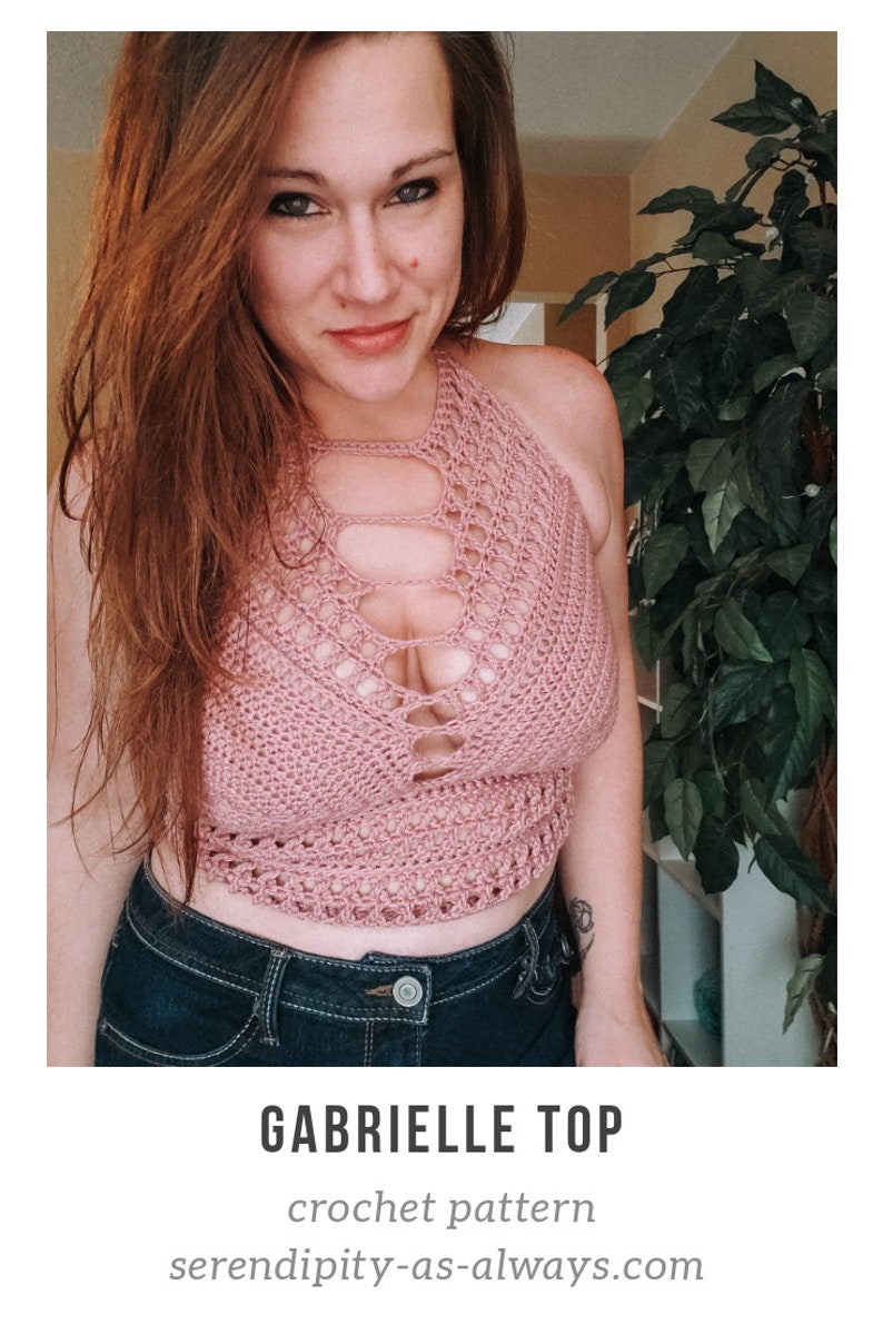 May include: A woman wearing a pink crochet halter top with a cutout design. The top is cropped and has a loose fit. The woman is also wearing blue jeans.