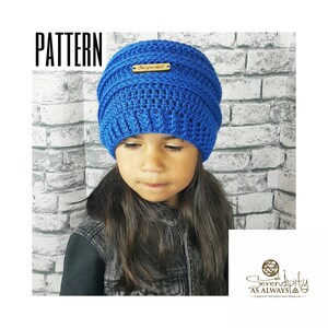 May include: A blue crocheted beanie with a wooden tag that says "Are you inspired?" The beanie is being worn by a child with long dark hair.