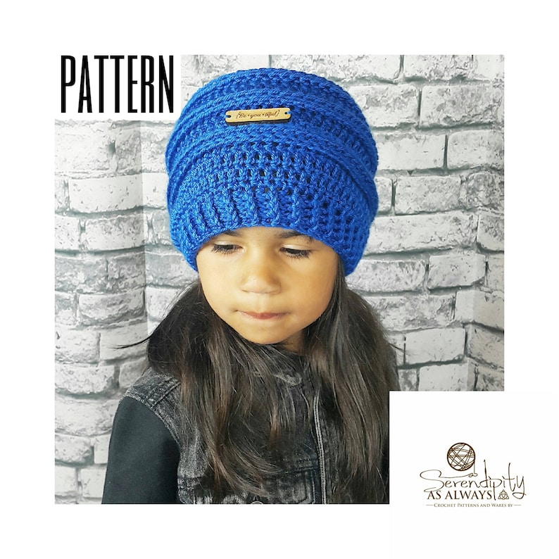 May include: A blue crocheted beanie with a wooden tag that says "Are you inspired?" The beanie is being worn by a child with long dark hair.