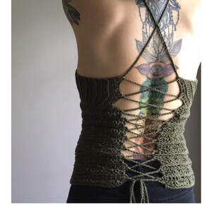 May include: A green crochet halter top with a lace-up back. The top is tied at the back with a long, thin cord. The top is worn by a person with a large tattoo on their back.