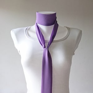 May include: A purple silk scarf tied in a knot around a white mannequin's neck. The scarf is long and flowing, with a simple design.