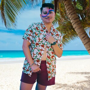 May include: A person wearing a white button-down shirt with a coconut print and maroon shorts. The person is standing in front of a tropical beach with palm trees.