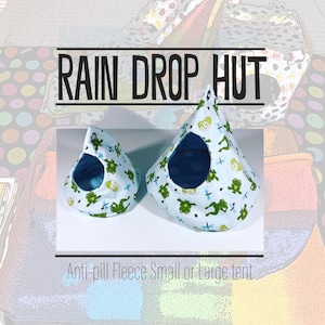 Könnte beinhalten: Zwei blaue und grüne Stoff-Tipis mit Frosch- und Libellenmotiven. Die Tipis sind mit "RAIN DROP HUT" und "Anti-pill Fleece Small or Large tent" beschriftet.