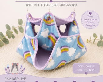 May include: A triple bunk hammock for small pets. The blue fleece cage accessory features a rainbow and cloud pattern. It has three cozy spaces and is easy to hang. The text says "Cozy, comfy, made for naps."
