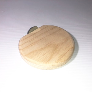 May include: A light-colored, wooden bottle stopper with a circular, flat design. A silver-colored metal piece is attached to the top. The stopper is designed to fit into the opening of a bottle.