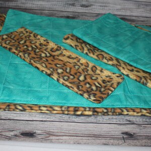 May include: A set of rectangular fabric mats featuring a combination of teal fabric with a subtle embossed swirl pattern and a brown and black leopard print fabric. The mats are layered, showing both the solid teal and the animal print textures.
