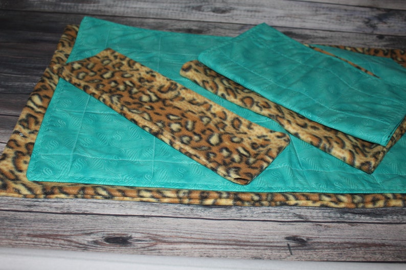 May include: A set of rectangular fabric mats featuring a combination of teal fabric with a subtle embossed swirl pattern and a brown and black leopard print fabric. The mats are layered, showing both the solid teal and the animal print textures.