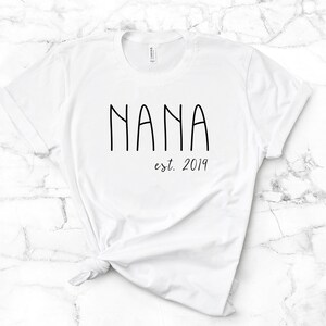 Peut inclure: T-shirt blanc avec un texte noir qui dit "NANA est. 2019".