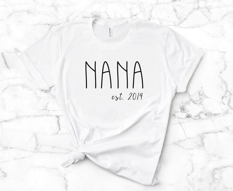 Peut inclure: T-shirt blanc avec un texte noir qui dit "NANA est. 2019".