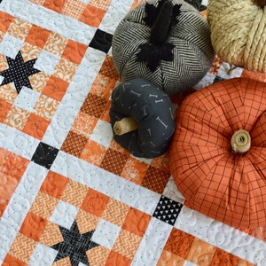 May include: A white and orange patchwork quilt with black stars and pumpkins. The quilt is quilted with a circular pattern.