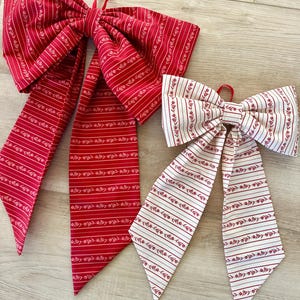 May include: Two fabric bows with red and white striped patterns and a floral design. The larger bow is red with white stripes and the smaller bow is white with red stripes.
