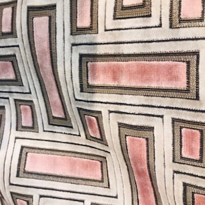May include: Close-up of a patterned fabric with a geometric design. The fabric features a repeating pattern of rectangles and squares in shades of pink, beige, and black. The design has a textured appearance, with a soft, velvety feel.
