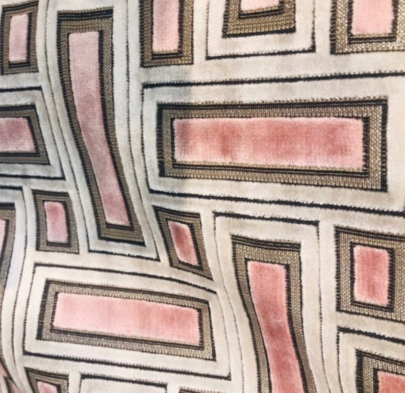 May include: Close-up of a patterned fabric with a geometric design. The fabric features a repeating pattern of rectangles and squares in shades of pink, beige, and black. The design has a textured appearance, with a soft, velvety feel.