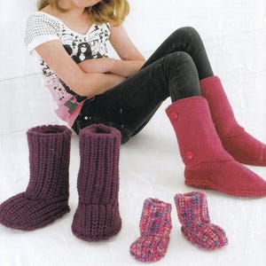May include: A selection of knitted boots in different sizes and colours. The image shows two pairs of adult-sized boots in deep purple and red-pink shades, plus a pair of smaller, multicoloured baby boots. The boots are made from thick yarn and have a ribbed texture.