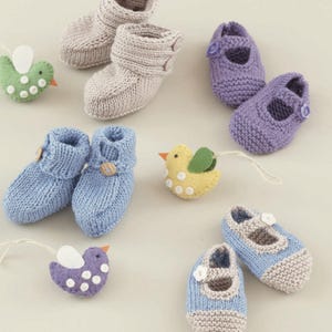 May include: A collection of handmade baby booties and shoes in various colors, including light blue, lavender, and beige. The knitted footwear features button closures and is accompanied by felt bird ornaments with white polka dots.