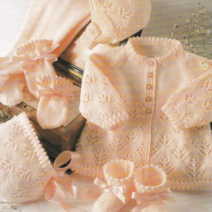 May include: A collection of soft, pale pink knitted baby clothes. The set includes a cardigan, bonnet, booties, mittens, and a blanket. Each item features a delicate leaf pattern and is tied with a matching pink ribbon. A charming ensemble for a newborn.
