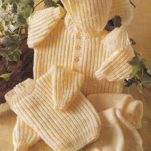 Op de afbeelding: Een lichtgele gebreide baby set, bestaande uit een trui met capuchon met knopen, een muts en bijpassende babyschoentjes. De set is gemaakt van ribgebreide stof.