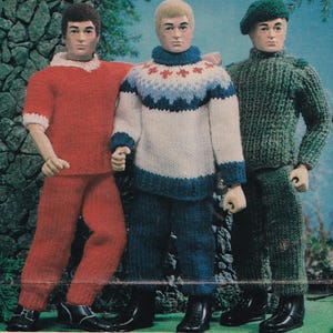 May include: Three dolls dressed in knitted outfits. One doll wears a red top and pants with white trim. Another doll is in a white sweater with blue and red patterns and blue pants. The third doll is in a green knitted outfit and a green beret.
