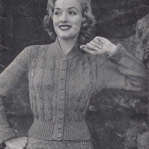 May include: A monochrome image of a woman in a knitted cardigan and skirt. The cardigan features a cable knit pattern and a button-up front. The skirt is a matching tweed-like material. The woman is smiling, with her hair styled in waves.