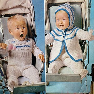 May include: Two babies in white knitted outfits with blue trim sit in prams. One baby is wearing a white knitted hat with blue trim. The babies are looking at the camera.