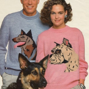 May include: Two people wearing sweaters with dog illustrations. The man is wearing a light blue sweater with a brown and black German Shepherd illustration. The woman is wearing a pink sweater with a brown and black bulldog illustration. A brown and black German Shepherd dog is standing in front of the couple.
