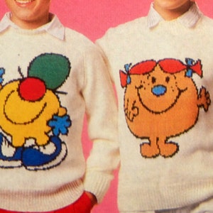 May include: Two white sweaters featuring cartoon characters. One sweater has a yellow character with a green hat and blue shoes. The other sweater has an orange character with red hair and blue shoes.